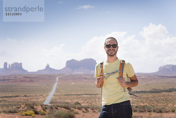USA  Utah  Porträt eines lächelnden Mannes mit Rucksack und Sonnenbrille auf dem Weg zum Monument Valley
