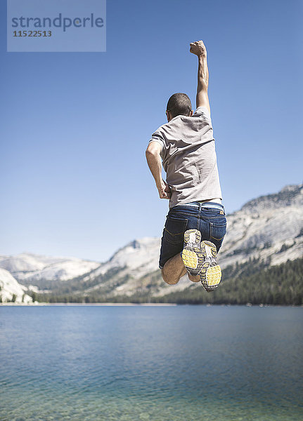 USA  Kalifornien  Yosemite Nationalpark  Rückansicht des in die Luft springenden Mannes am Bergsee
