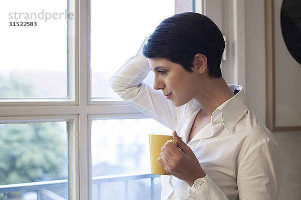 Frau hält eine Tasse Kaffee und schaut aus dem Fenster.