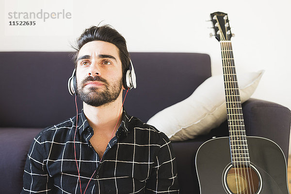 Junger Mann zu Hause mit Kopfhörer neben der Gitarre