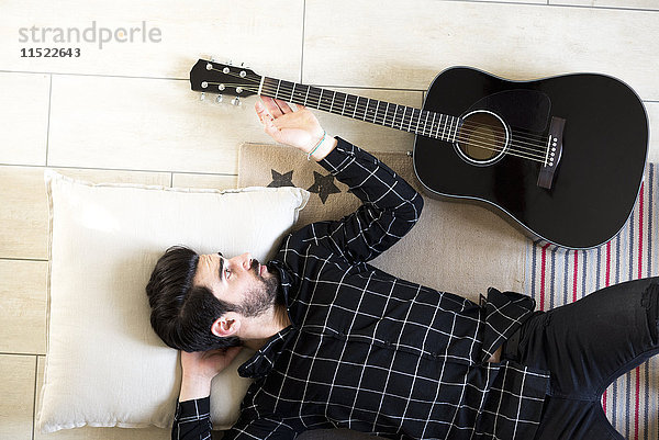 Junger Mann zu Hause auf dem Boden neben der Gitarre liegend