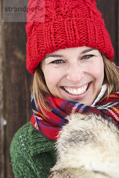 Porträt einer glücklichen Frau mit rotem Bommelhut im Winter