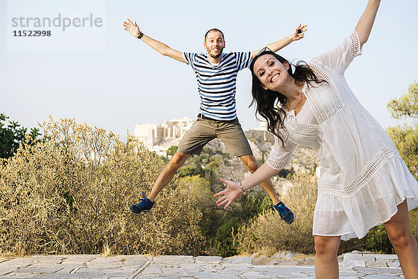 Griechenland  Athen  glückliches Paar beim Springen auf Areopagus mit der Akropolis und Parthenon im Hintergrund