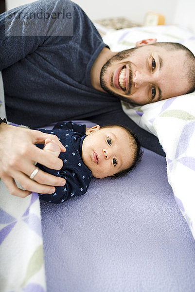 Glücklicher Vater liegt mit seinem neugeborenen Mädchen im Bett.