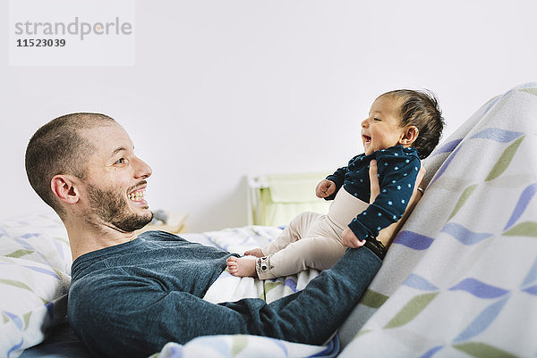 Glücklicher Vater  der mit seinem neugeborenen Mädchen im Bett liegt.