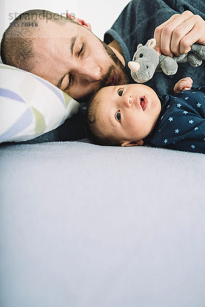 Vater spielt mit seinem neugeborenen Mädchen und einem Kuscheltier auf dem Bett.