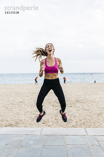 Junge sportliche Frau beim Springen am Strand  lachend