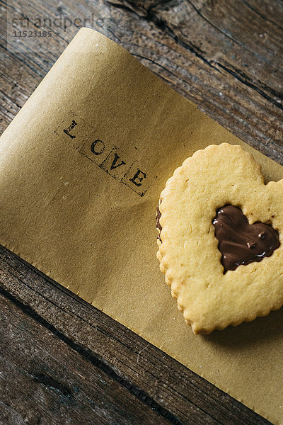 Herzförmiges Mürbegebäck mit Schokoladenfüllung auf Papier mit dem Wort Liebe .
