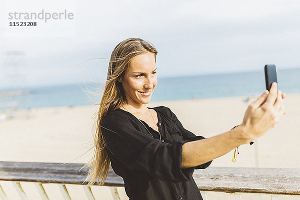 Lächelnde junge Frau mit einem Selfie am Strand