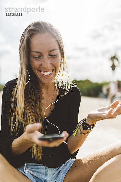 Glückliche junge Frau mit Handy und Ohrhörern im Freien