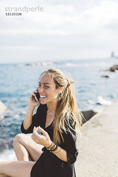 Glückliche junge Frau an der Strandpromenade am Handy