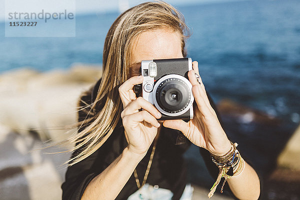 Junge Frau fotografiert mit altmodischer Kamera an der Strandpromenade