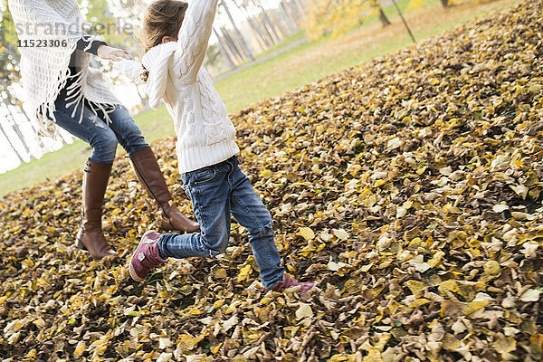 Mädchen läuft mit Mutter in herbstlichen Blättern