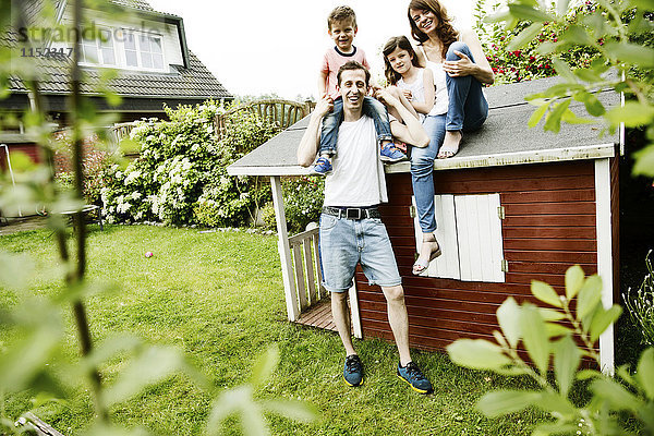 Glückliche Familie sitzt auf dem Dach ihres Gartenschuppens