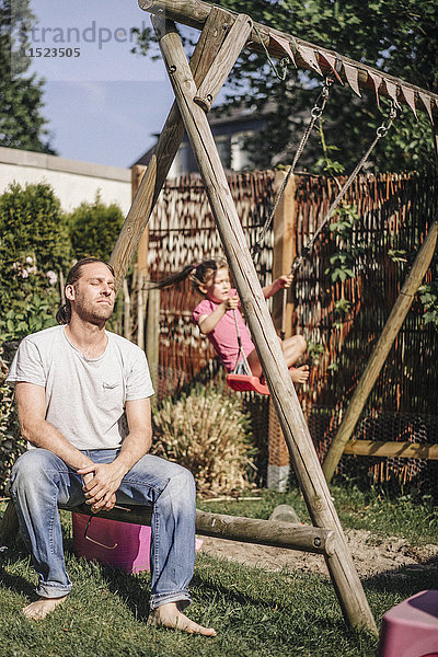 Erschöpfter Vater im Garten mit Tochter auf Schaukel