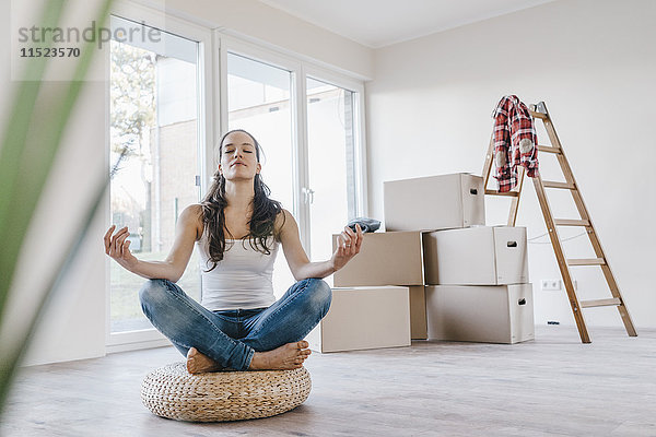 Frau sitzend auf Kissen in ihrer neuen Wohnung  meditierend