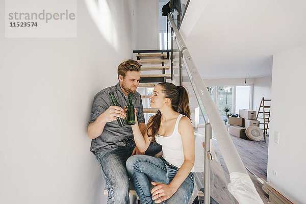 Paar im neuen Zuhause auf der Treppe sitzend  Toast mit Bierflaschen