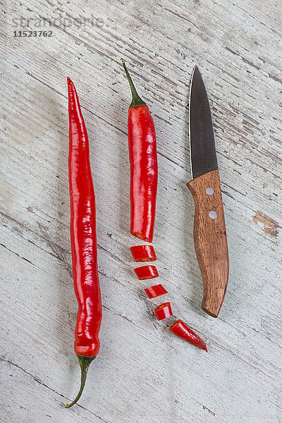 Ganze und geschnittene rote Chilischote und ein Küchenmesser auf Holz