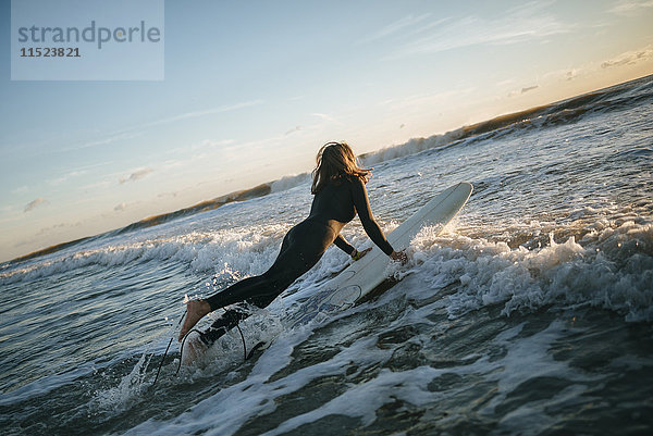 Surferin im Neoprenanzug mit Surfbrett ins Meer gekleidet