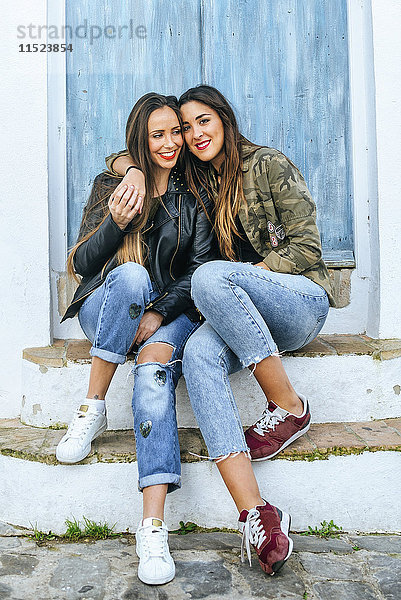 Zwei lächelnde junge Frauen sitzen auf einer Buckelpiste und umarmen sich.