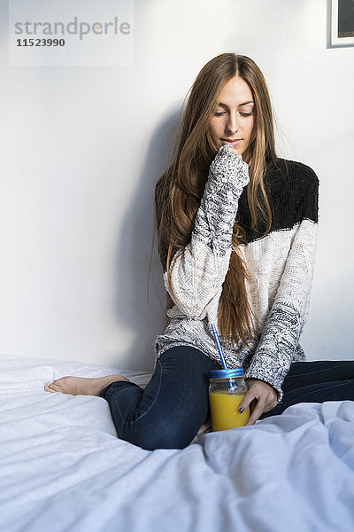 Junge Frau auf dem Bett sitzend mit hausgemachtem Getränk