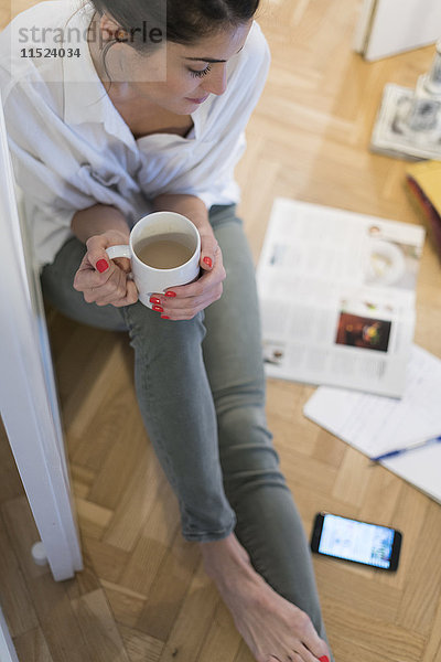 Junge Frau sitzt auf dem Boden und trinkt weißen Kaffee.