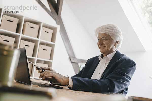 Lächelnder Senior-Geschäftsmann mit Laptop in seinem Büro