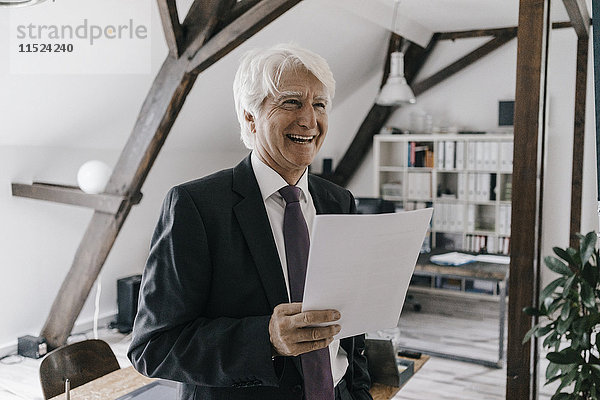 Porträt eines lächelnden Geschäftsmannes mit Dokument in seinem Büro