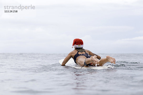 Indonesien  Bali  Frau auf dem Surfbrett mit Weihnachtsmütze