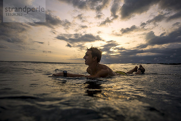 Indonesien  Bali  Surfer bei Sonnenuntergang auf dem Surfbrett liegend