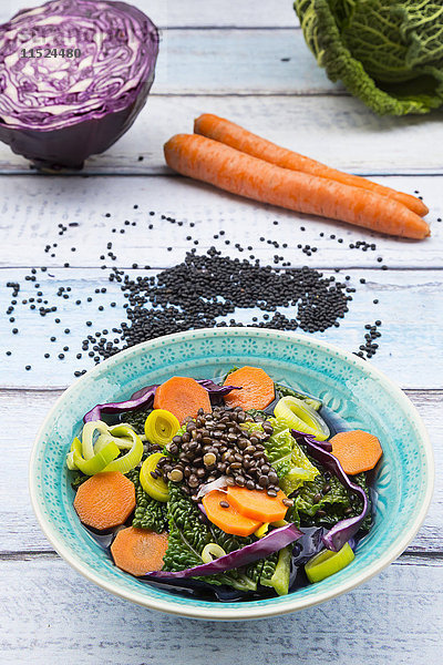 Schale mit veganem Kohlragout mit Linsen und Zutaten auf Holz