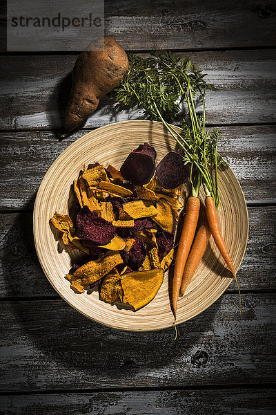Gemüsechips aus Karotten  Süßkartoffeln und Rote Beete auf Teller und dunklem Holz