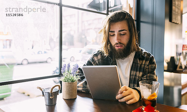 Stilvoller junger Mann mit Tablette im Cafe