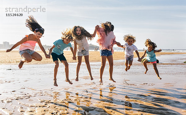 Gruppe von sechs Kindern beim Springen in der Luft am Strand