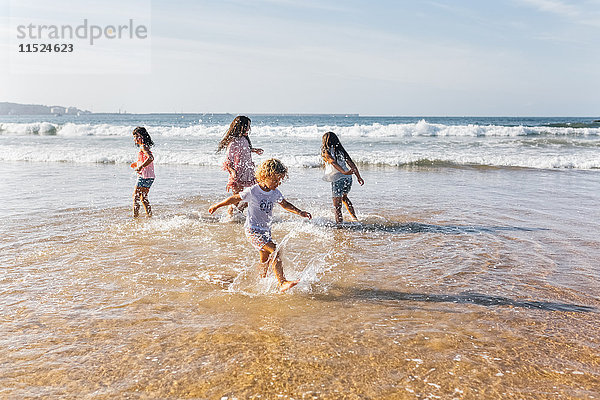 Vier Kinder planschen mit Wasser am Meer