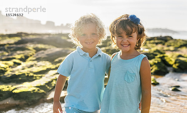 Portrait eines glücklichen kleinen Jungen und Mädchens Seite an Seite am Strand