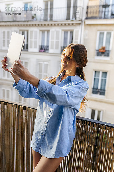 Junge Frau steht auf dem Balkon und nimmt Selfie mit digitalem Tablett