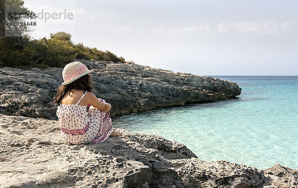 Mädchen am Strand sitzend mit Blick aufs Meer
