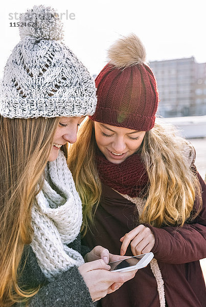 Zwei Teenagermädchen mit Pudelmützen und Schals auf dem Smartphone