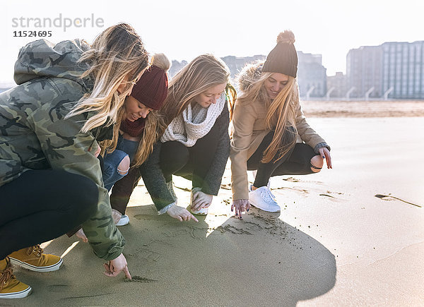 Vier Freunde beim Zeichnen im Sand am Strand