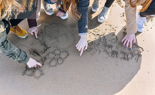 Vier Freunde beim Zeichnen im nassen Sand am Strand  Teilansicht