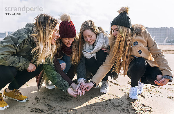 Vier Freunde  die sich am Strand die Hände reichen.