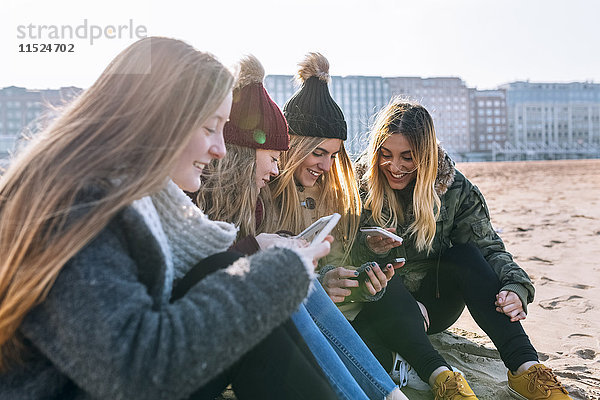 Vier Freunde  die am Strand sitzen und SMS-Nachrichten senden