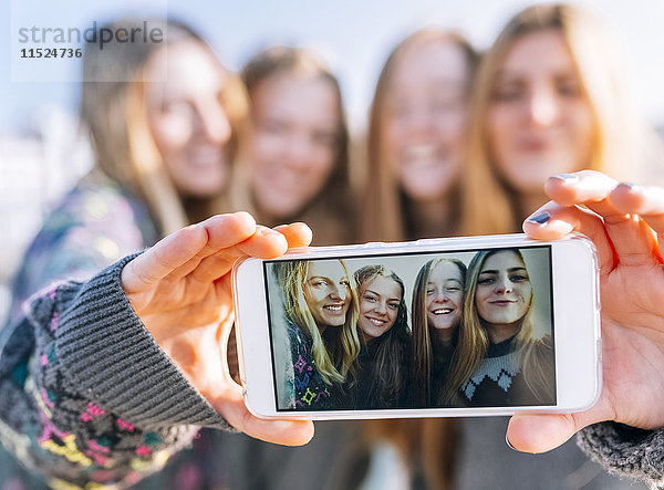 Gruppenbild von vier Freunden auf dem Display des Smartphones  Nahaufnahme