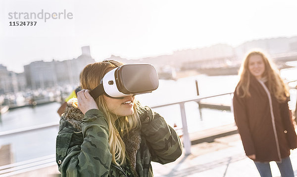 Teenager-Mädchen  das eine VR-Brille trägt  während ihre Freundin sie beobachtet.