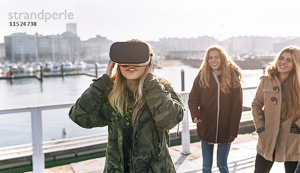 Teenager-Mädchen  das eine VR-Brille trägt  während ihre Freunde sie beobachten.