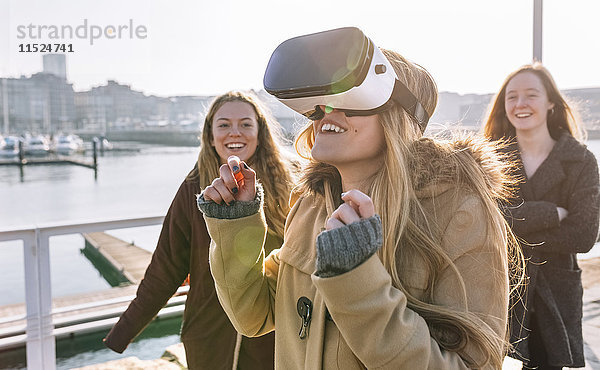 Teenager-Mädchen  das eine VR-Brille trägt  während ihre Freunde sie beobachten.