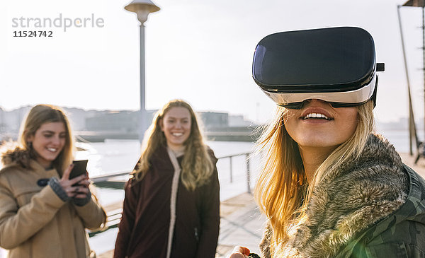 Teenager-Mädchen  das eine VR-Brille trägt  während ihre Freundin sie beobachtet.