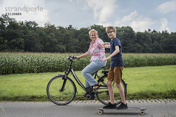 Enkel und Großmutter fahren gemeinsam Fahrrad und Skateboard