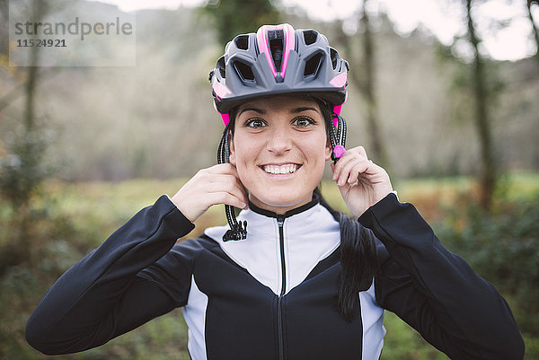 Porträt einer lächelnden Frau beim Aufsetzen des Fahrradhelms